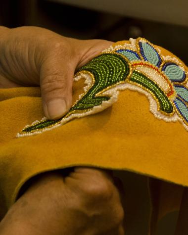 Hands hold beading work up to tanned hide