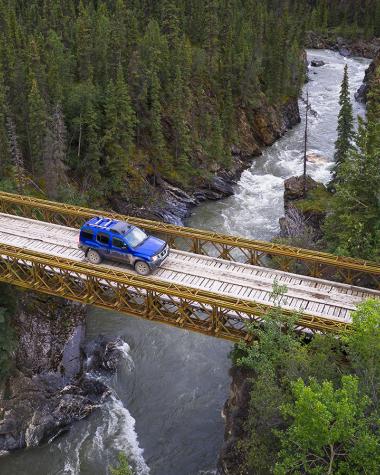 A blue car drives across a bridge above a river canyon