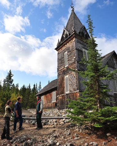 Three people in front of Saint Andrews Church in Fort Selkirk